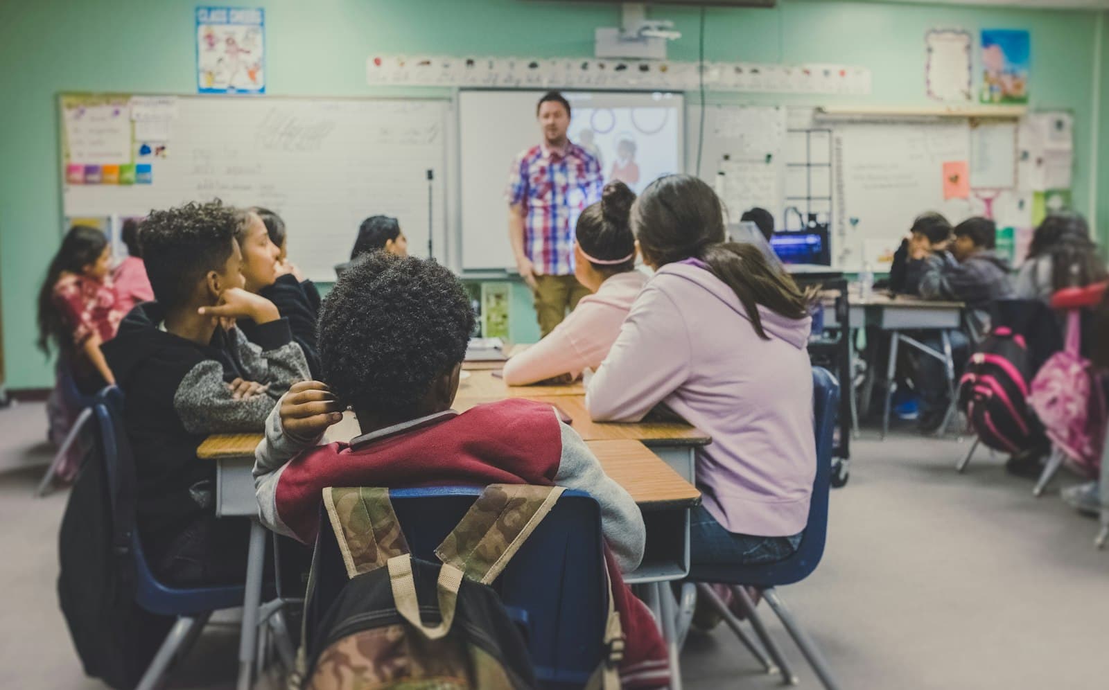 A teacher at the front of a classroom with students sitting at group tables