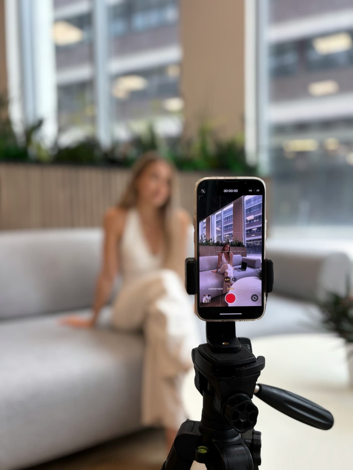 A creator on a sofa filming herself with a phone on a tripod