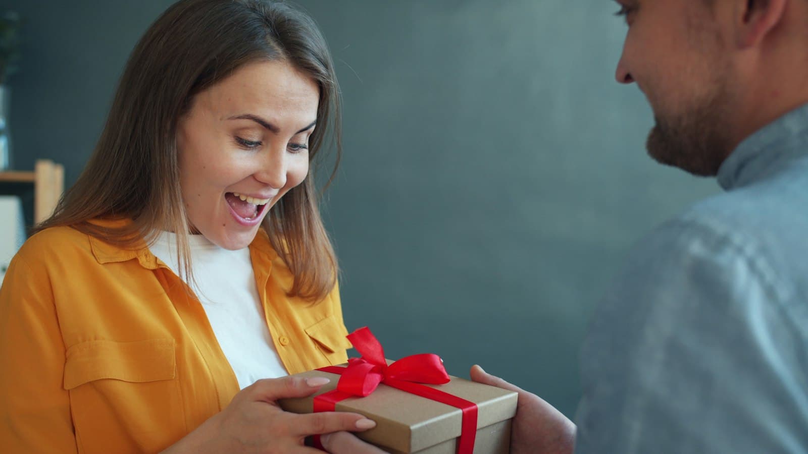 A woman smiling as a friend hands her a wrapped gift with a red ribbon